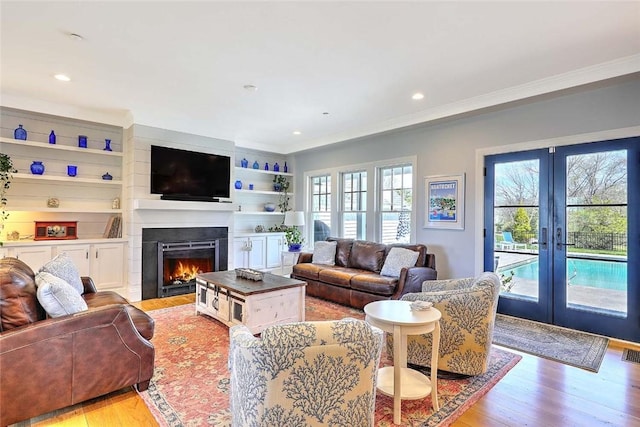 living room with a lit fireplace, french doors, visible vents, light wood finished floors, and ornamental molding