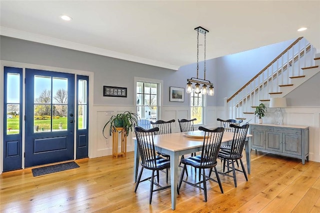 dining space featuring wainscoting, a decorative wall, light wood-style floors, stairway, and a notable chandelier