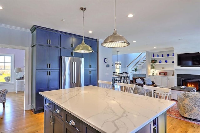 kitchen with high end refrigerator, light stone counters, open floor plan, ornamental molding, and light wood-style flooring