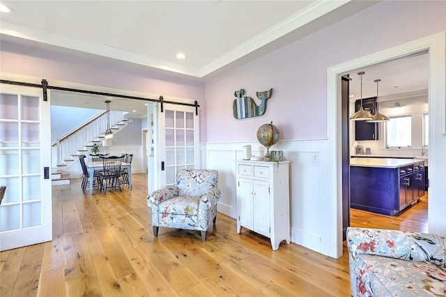 sitting room featuring crown molding, wainscoting, light wood finished floors, and a barn door