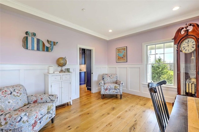 sitting room with ornamental molding, light wood finished floors, a decorative wall, and a wainscoted wall
