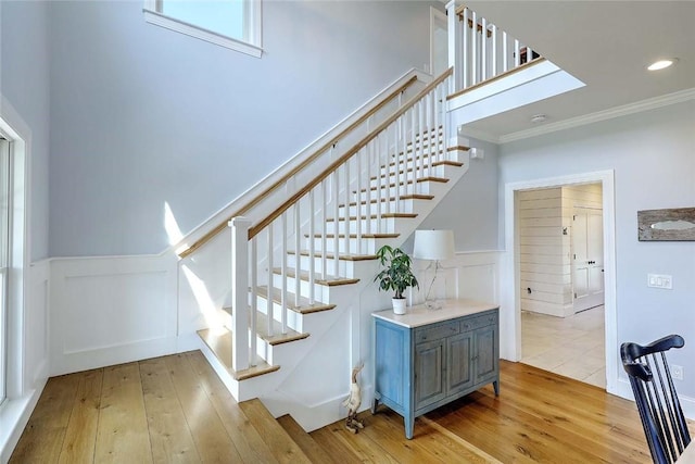staircase featuring crown molding, a decorative wall, wood-type flooring, and wainscoting