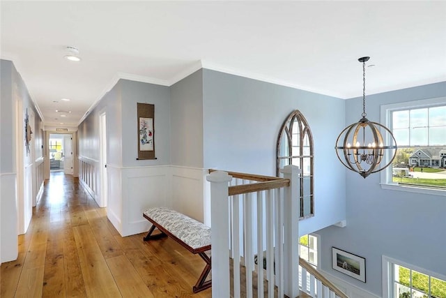 corridor featuring crown molding, a notable chandelier, a wainscoted wall, light wood finished floors, and an upstairs landing