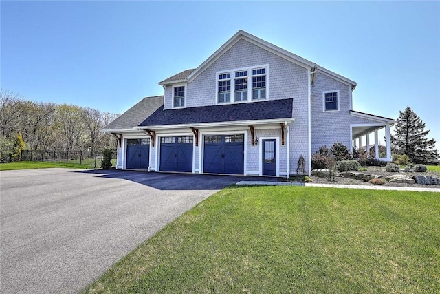 view of front of house featuring roof with shingles, a front yard, fence, aphalt driveway, and an attached garage