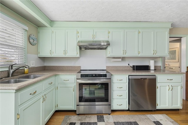 kitchen with appliances with stainless steel finishes, wood finished floors, under cabinet range hood, and a sink