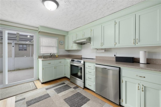 kitchen with a sink, under cabinet range hood, light wood-style floors, a textured ceiling, and appliances with stainless steel finishes
