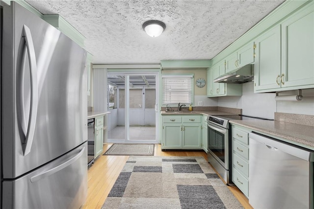 kitchen featuring light wood-style flooring, green cabinetry, stainless steel appliances, under cabinet range hood, and a sink