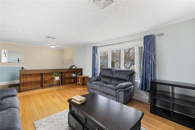 living room featuring a textured ceiling, visible vents, light wood-type flooring, and baseboards