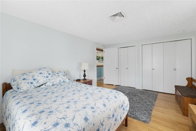 bedroom featuring visible vents, multiple closets, and light wood-style flooring