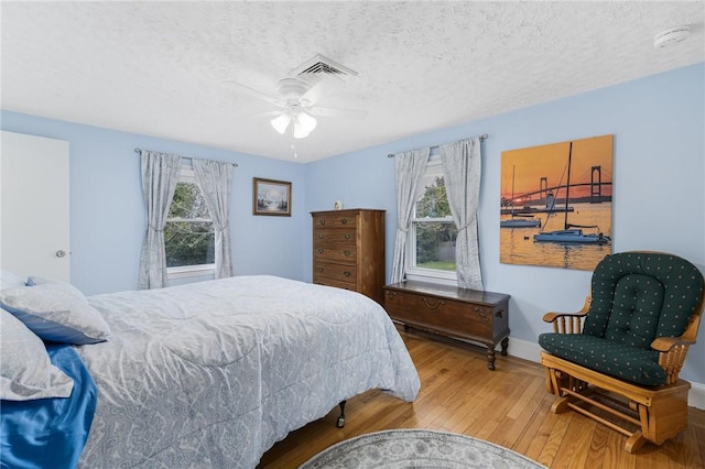 bedroom featuring wood finished floors, visible vents, ceiling fan, and a textured ceiling