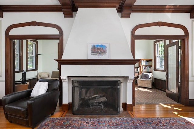 living room featuring wood finished floors, plenty of natural light, crown molding, a large fireplace, and beamed ceiling