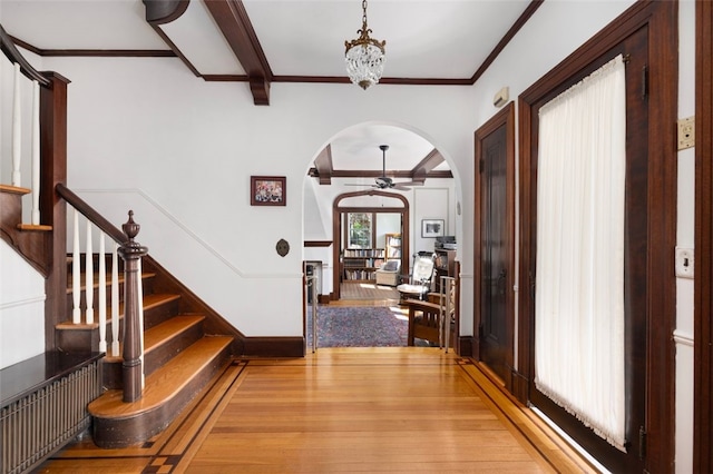 entryway featuring arched walkways, ceiling fan, ornamental molding, wood-type flooring, and stairs