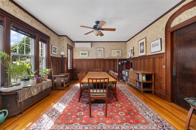 dining area with wood finished floors, wainscoting, ceiling fan, ornamental molding, and a wall unit AC