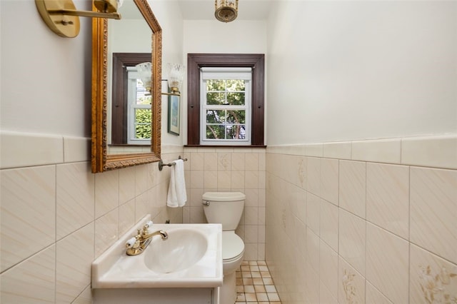 half bathroom with toilet, tile walls, a sink, and wainscoting
