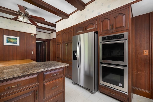kitchen featuring appliances with stainless steel finishes, wallpapered walls, beam ceiling, ceiling fan, and dark stone countertops