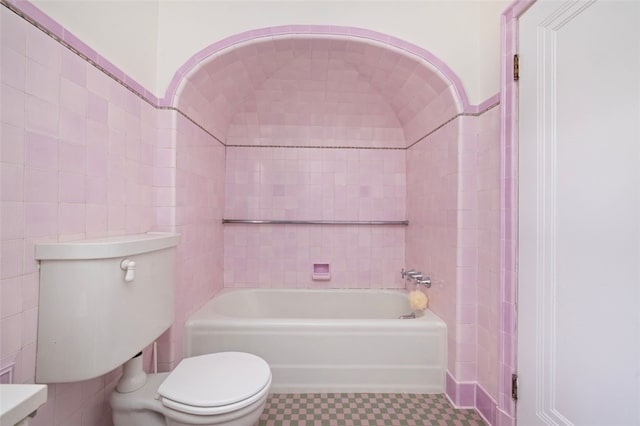 bathroom featuring toilet, a tub to relax in, and tile walls