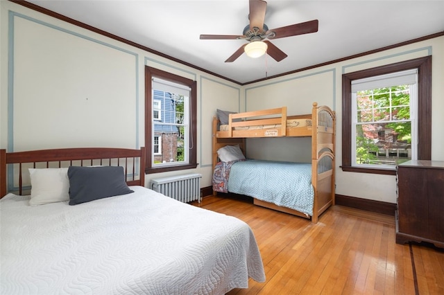 bedroom featuring radiator, light wood finished floors, ornamental molding, baseboards, and a ceiling fan
