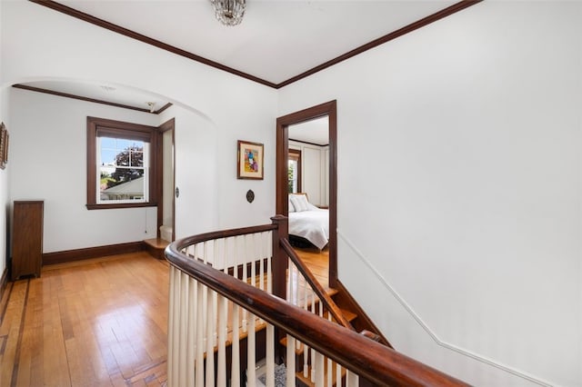 hall with healthy amount of natural light, arched walkways, ornamental molding, baseboards, and light wood-style flooring