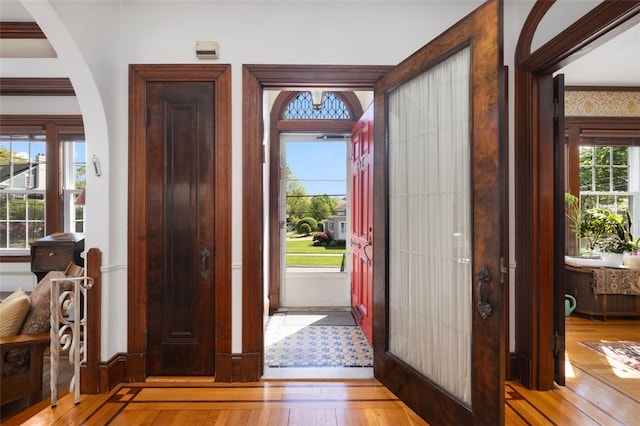 foyer entrance with light wood-style flooring, arched walkways, and baseboards