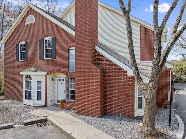 view of front facade featuring brick siding, a shingled roof, and a chimney