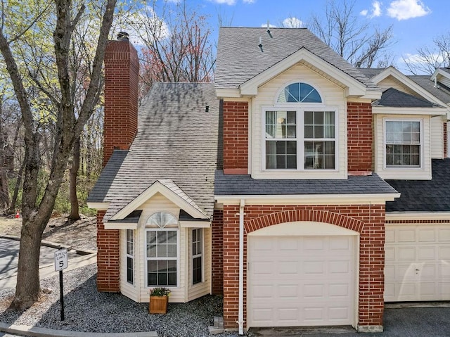 view of front facade with a chimney, brick siding, an attached garage, and roof with shingles