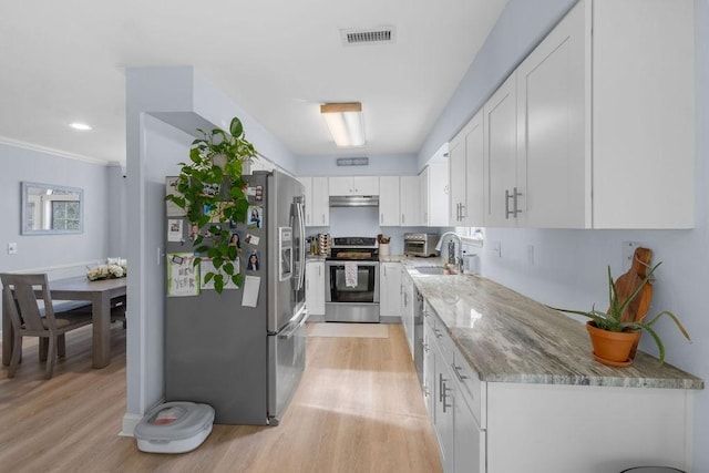 kitchen with light wood finished floors, a sink, stainless steel appliances, light stone counters, and white cabinets