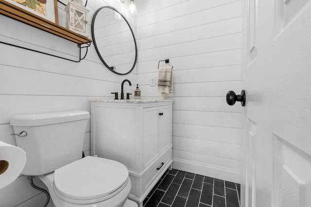 bathroom with wood walls, toilet, tile patterned flooring, and vanity
