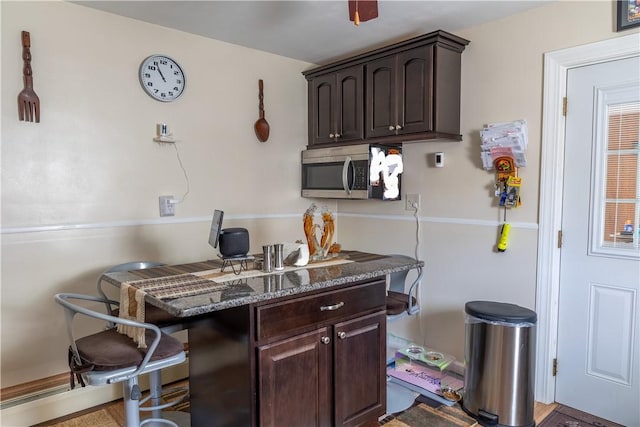 132 Bakers Creek Rd, Warwick, RI 02886 - kitchen featuring dark stone counters, dark brown cabinets, stainless steel microwave, and a kitchen bar