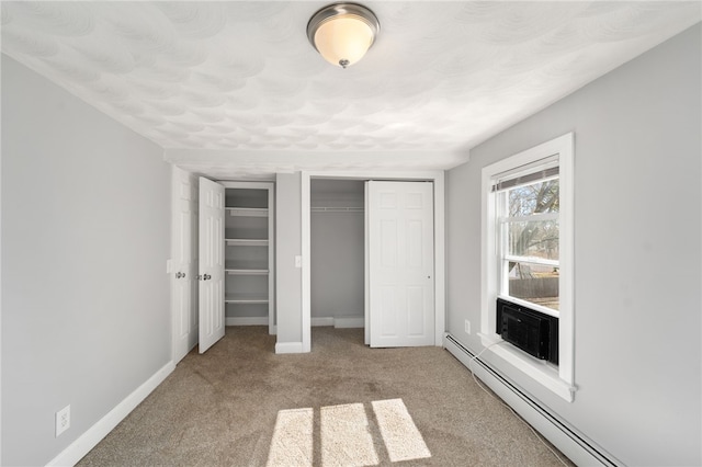 unfurnished bedroom with carpet, baseboard heating, multiple closets, and baseboards