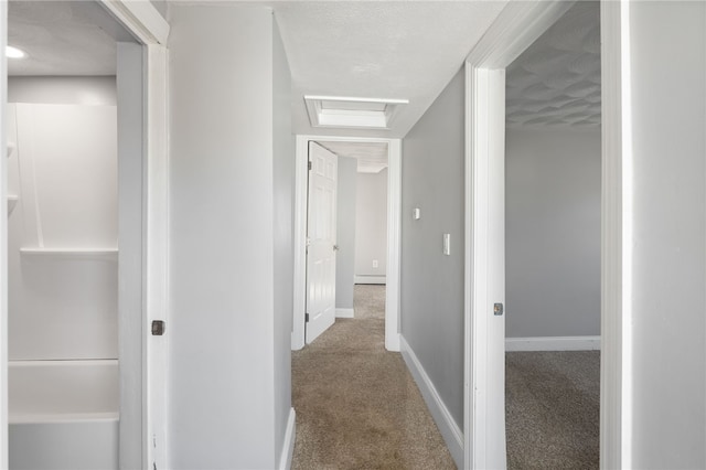 hall with attic access, a baseboard radiator, carpet floors, and baseboards