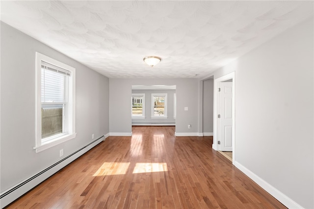 empty room with a baseboard radiator, light wood-type flooring, baseboard heating, and baseboards