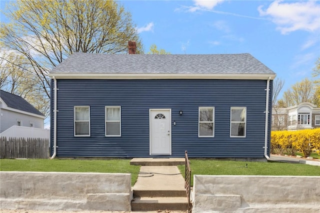 view of front of house featuring roof with shingles, fence, a front yard, and a chimney