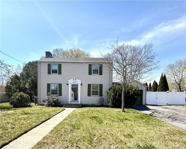 colonial home featuring aphalt driveway, fence, a front yard, a chimney, and a gate