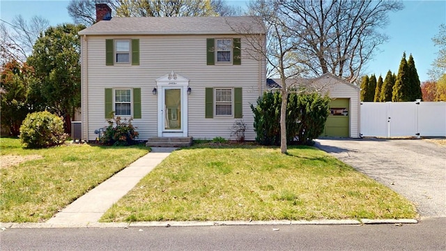 colonial house featuring a chimney, a garage, fence, aphalt driveway, and a front lawn