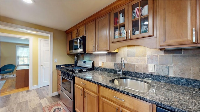 kitchen with glass insert cabinets, stainless steel gas range, light wood-type flooring, dark stone counters, and a sink