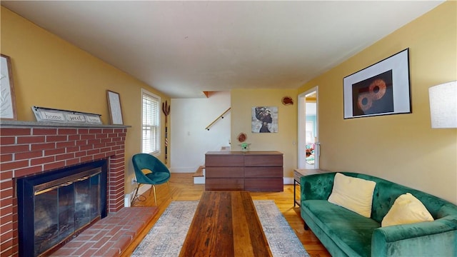 living room featuring baseboards, a brick fireplace, wood finished floors, and stairway