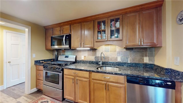 kitchen with light wood-type flooring, a sink, dark stone countertops, glass insert cabinets, and stainless steel appliances