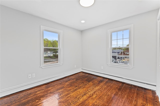 spare room featuring a healthy amount of sunlight, baseboards, a baseboard heating unit, and dark wood finished floors