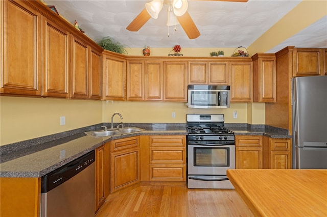 kitchen with brown cabinetry, stainless steel appliances, light wood finished floors, a sink, and a ceiling fan