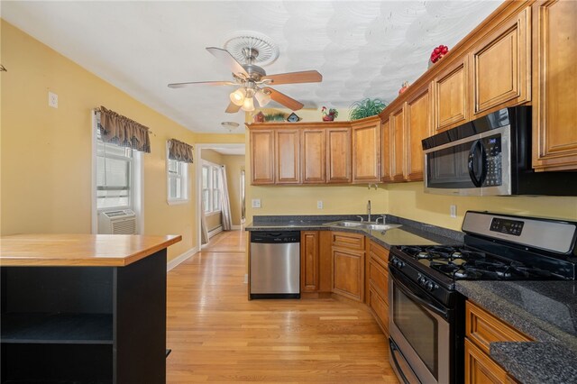 kitchen with brown cabinets, a sink, appliances with stainless steel finishes, light wood-style floors, and a ceiling fan