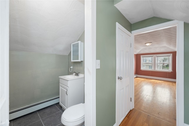 half bath with lofted ceiling, toilet, vanity, and baseboard heating