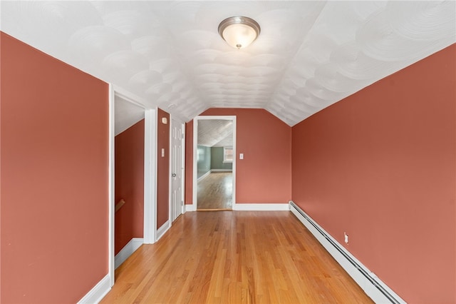 additional living space with lofted ceiling, light wood-style flooring, a baseboard heating unit, and baseboards