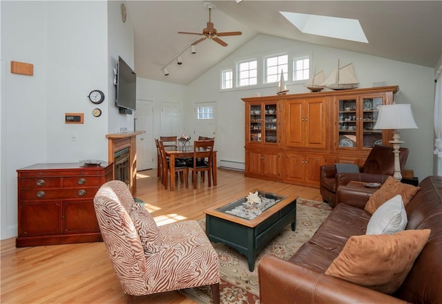 living area with a skylight, baseboard heating, ceiling fan, light wood finished floors, and high vaulted ceiling