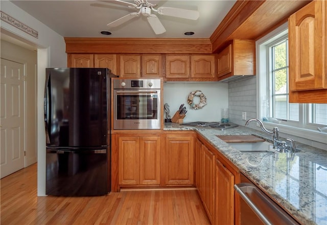 kitchen with light stone countertops, stainless steel appliances, light wood-style flooring, and a sink
