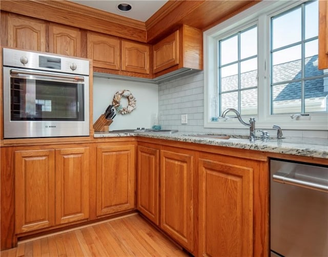 kitchen featuring light stone counters, brown cabinets, a sink, stainless steel appliances, and light wood finished floors