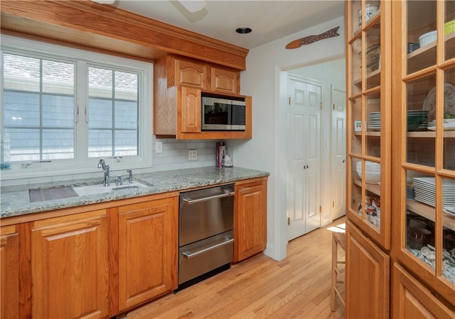 kitchen featuring glass insert cabinets, light wood finished floors, a sink, and stainless steel appliances