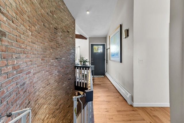 corridor with brick wall, vaulted ceiling, baseboards, a baseboard heating unit, and light wood-style floors