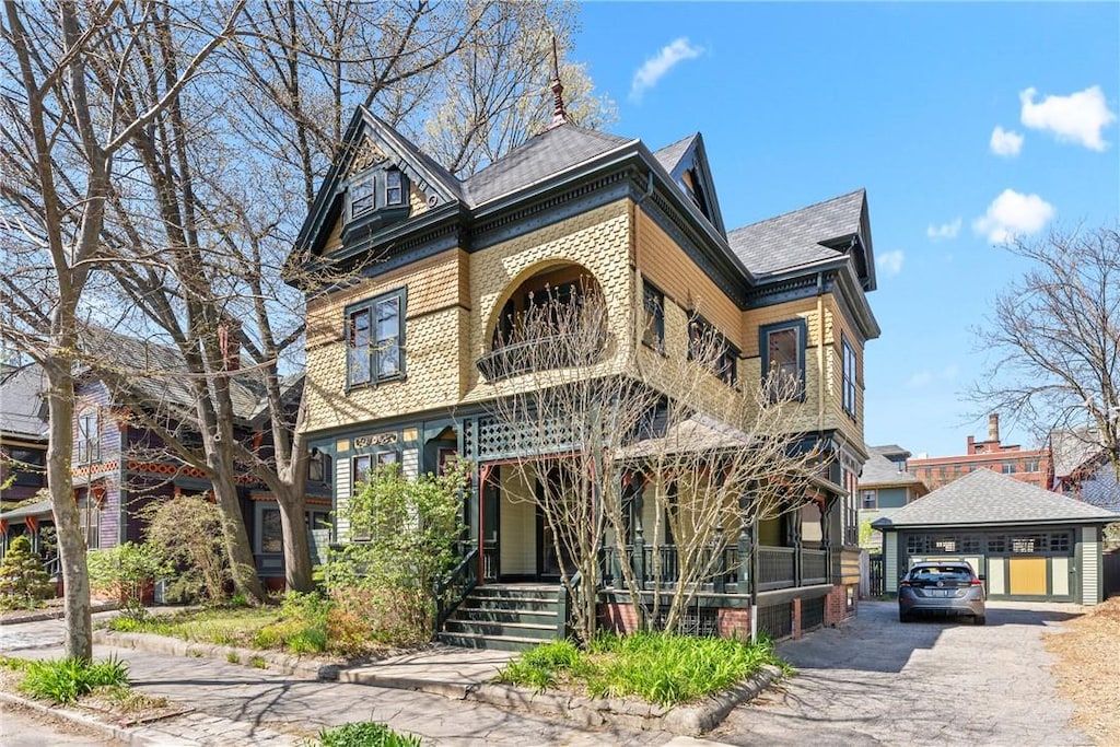 victorian-style house with a porch, an outdoor structure, and a shingled roof