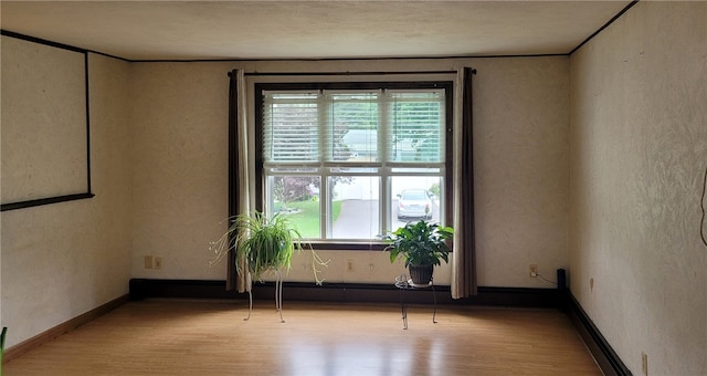 empty room featuring wood finished floors, a textured wall, and baseboards