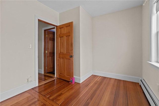 empty room with baseboards, a baseboard heating unit, and wood-type flooring